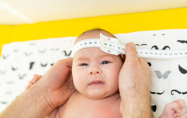 Shot of a pediatrician examining newborn baby. Doctor using measurement tape checking baby's head...