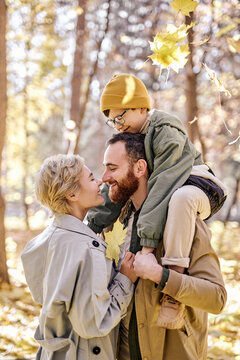 nice caucasian family with child on walk in pard at day time, sunny warm weather. romantic married couple in love, child boy sits on shoulders of father. family, childhood, lifestyle concept