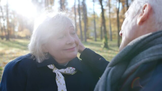 Senior man saying compliments to his beautiful wife sitting on bench in park