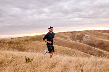 athletic runner man in black tracksuit running on field training for marathon run doing high intensity interval training sprint workout outdoors. caucasian sports model fit and healthy aspirations.