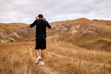 Rear view Sportsman is walking in field among mountains after jogging, take a break, deeply breathing, after dynamic active training on long distance. intense workout, sport, fitness concept