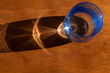 vaso de cristal con agua sobre mesa de madera que hace una sombla con reflejo