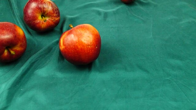 Ripe red apples roll on a green silk textile, slow motion