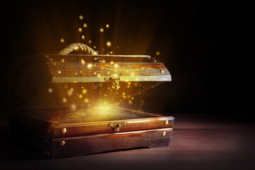 Open treasure chest with gold coins on wooden table against black background