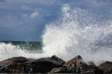 Ocean water splash on rock beach with beautiful sky and clouds. Sea wave splashing on stone at sea shore.