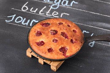 Sour cherry cake in a pan on a wooden trivet. Ingredients written in chalk on the background.