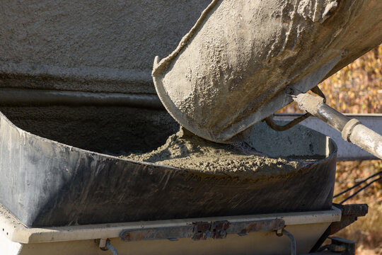 Pouring concrete at a construction site. The concrete is poured into the loading hopper of the concrete pump from the concrete mixer guide chute. The process of pouring the foundation in a building.