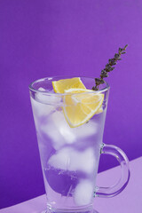 Close-up on cold drink with ice, lemon and lavender flower in the drinking glass on the purple...