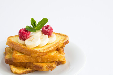 Close-up on french toasts with banana and raspberry on the white plate on the white background....