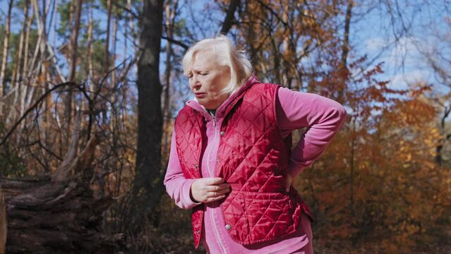 Aged woman suffering lower back pain while running in park, problems with spine