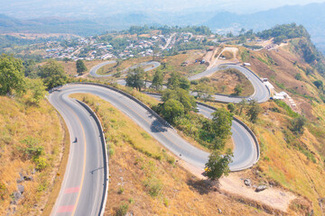 Aerial view of cars driving on curved, zigzag curve road or street on mountain hill with green natural forest trees in rural area of Nan, Thailand. Transportation.