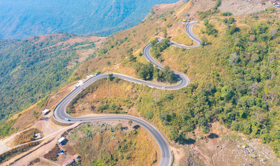 Aerial view of cars driving on curved, zigzag curve road or street on mountain hill with green natural forest trees in rural area of Nan, Thailand. Transportation.