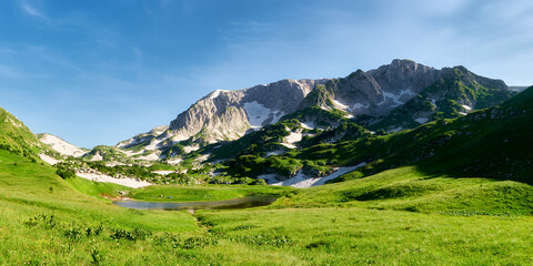 Tent camp on the green flowering shore of a mountain lake surrounded by mountain peaks