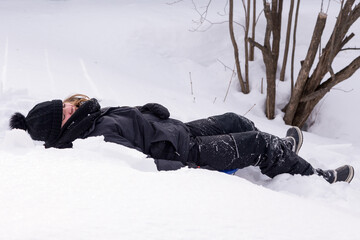 Horizontal portrait of little girl in snowsuit lying down outdoors in winter with eyes closed