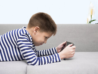 The child looks at the tablet, the gadget is lying on the couch. Leisure time concept.