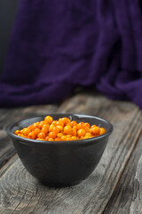 orange sea buckthorn berries on wooden table. and purple background , copy space