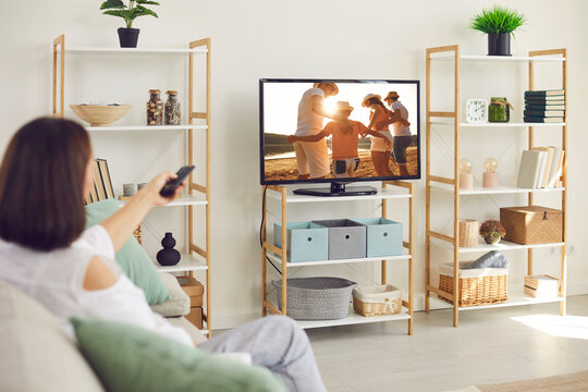 Woman watching film on television at home. Relaxed lady sitting on sofa in living room, watching movie, series, serial or collection of photo memories of family summer holiday on big widescreen TV set