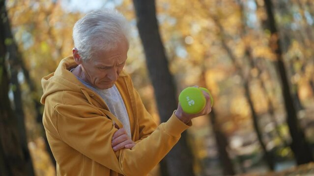 Aged man in sports wear lifting dumbbell, feeling elbow pain, arthritis, cramps