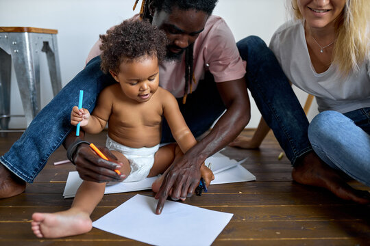 Young black family man and woman sitting on floor with child girl daughter drawing picture, painting. at home. at day time, weekends, holidays concept. creative free time, happy childhood.