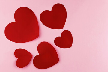 Five red hearts on pink pastel paper textured background. Top view. Flat lay. Close up. Text copy space.