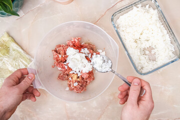 A man adds boiled rice to the minced meat for the lazy cabbage rolls on the table.