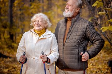Romantic aged caucasian couple enjoying the moment of love in park, nordic walking at autumn day...