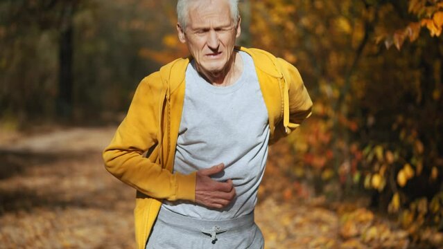 Senior man running in park, feeling acute pain in spine, suffering old injury