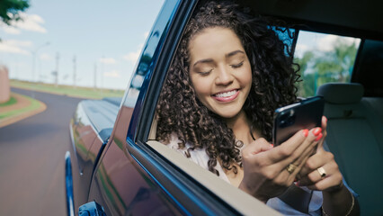 Beautiful Latin woman tourist traveling in a taxi and rewritten with your friends on your smartphone