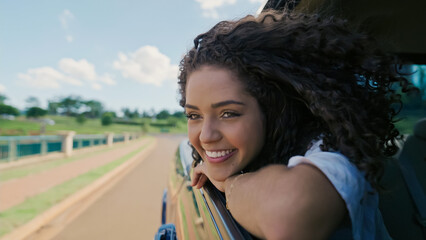 Latin woman in car window. Car trip. Curly hair in wind. Girl looks out of car window.