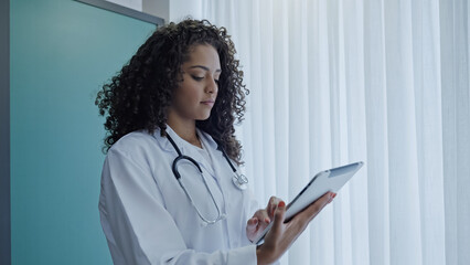 Latin young female doctor wear white uniform, using digital tablet in hospital