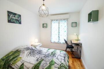 Tropical spirit bedroom with green bed. Wooden desk and black chair. (France - 13.06.2019)