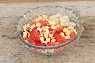 A salad that contains ingredients such as tomatoes and cheese - wooden background
