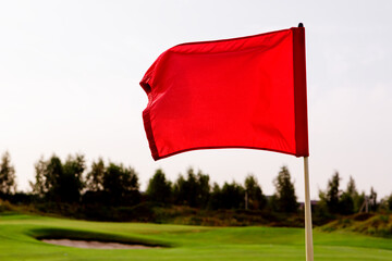 A red flag is fluttering in the wind over the golf course.