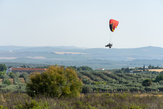 Side view of a powered Parachute. Ultralight Paramotor vehicle flying in the sky with houses. green and mountains behind