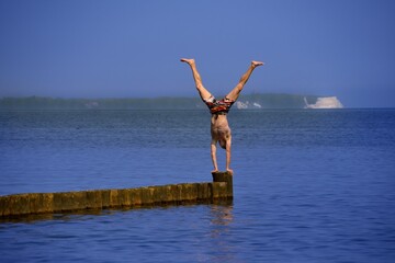 young athletic man doing handstand on breakwater at the baltic sea