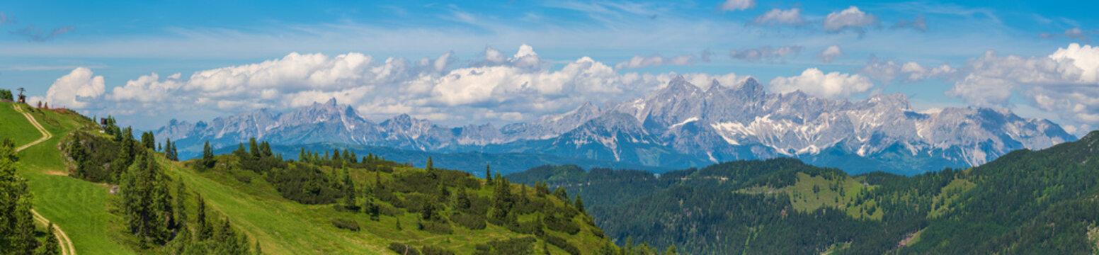 Beautiful view of alpine mountain scenery, blooming green meadows, snowcapped mountain peaks, mountain cable car station. The sunny day with blue sky in summer.