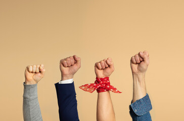 Four male hands on a beige background showing a fist, symbol of the feminist movement.