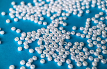 Selective focus, white pearl beads for needlework on a blue background. Making jewelry from beads, embroidery, mosaic and knitting