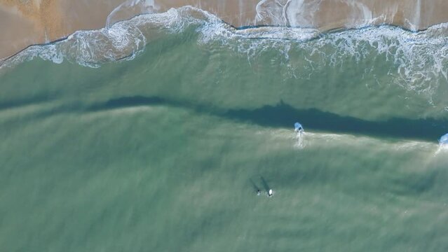 An aerial view of surfers and waves at Boscombe beach in Bournemouth on a sunny winter's day.