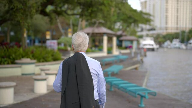 Walking behind a businessman by the river. 4k tracking focus