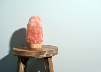 Himalayan salt lamp on wooden table near neutral wall with copy space