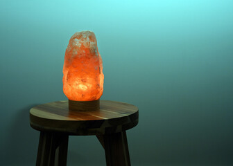 Himalayan salt lamp glowing on wooden table near turquoise wall at night with copy space