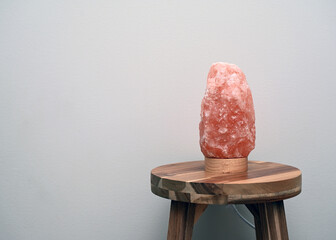 Himalayan salt lamp on wooden table near neutral wall with copy space