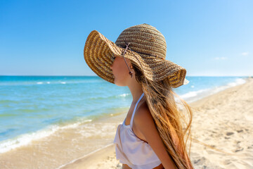 Summer, beautiful little girl in a straw hat is resting on the beach sea