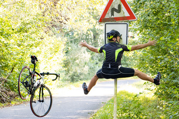 A falling cyclist bumps into a road sign warning about road with turns. - obrazy, fototapety, plakaty