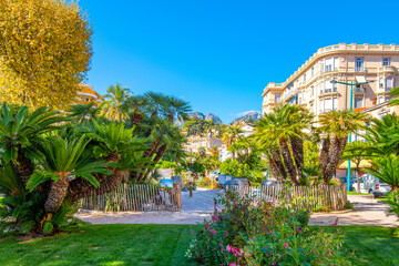 The Alpes Maritimes mountains rise behind the Jardins Bioves in the city center of the seaside resort city of Menton, France, on the French Riviera.	 - obrazy, fototapety, plakaty