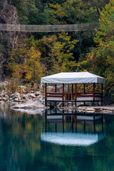 autumn mountain landscape with shady lake, picnic gazebo and hanging bridge