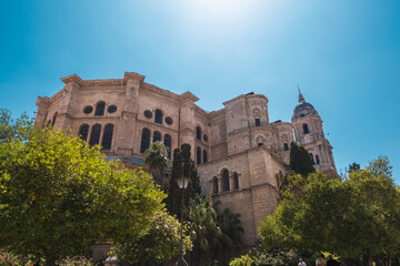 Fototapeta na wymiar Froschblick auf südeuropäische Kirche mit Bäumen vor klarem, blauem Himmel | Malaga, Spanien