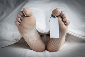 Close-up of the feet of a corpse covered in a sheet; with a blank tag tied on the big toe of the...