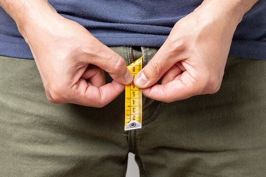 Close up of a young man holding a short piece of measuring tape that is popping up from the fly of his blue jeans